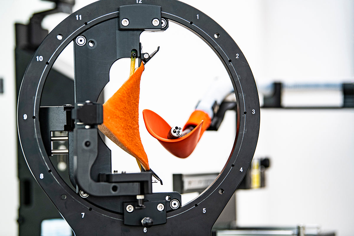An unlit surgical endoscope rests on the orange spatular representing the fundum. This is the frontal view of the G-Master ESD training system. The round setting gate has a sheet of plant-based tissue installed on the left, stretched to replicate a specific point on the gastric wall.