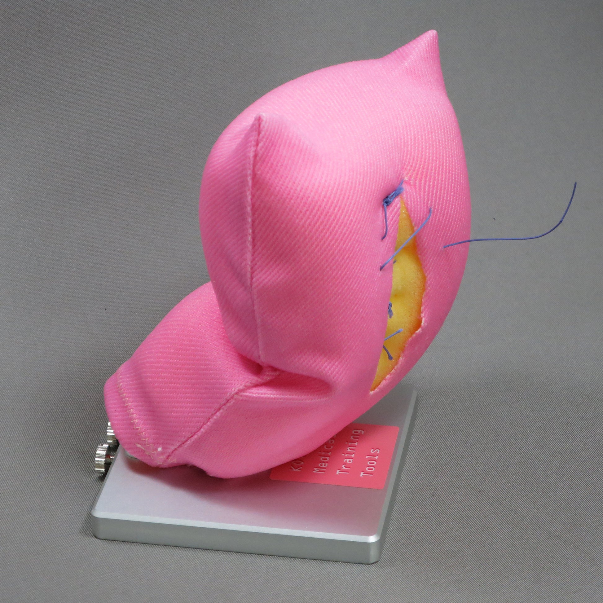 Sutures and an incision on the Laparoscopic Myectomy training model. Yellow foam can be seen through an incision in the pink fabric.