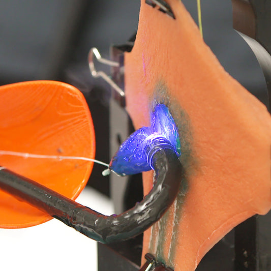 A surgical endoscope resects a circular section of the Gastric Mucosa Model. Blue injection solution drips out of the incision over the simulated gastric wall.