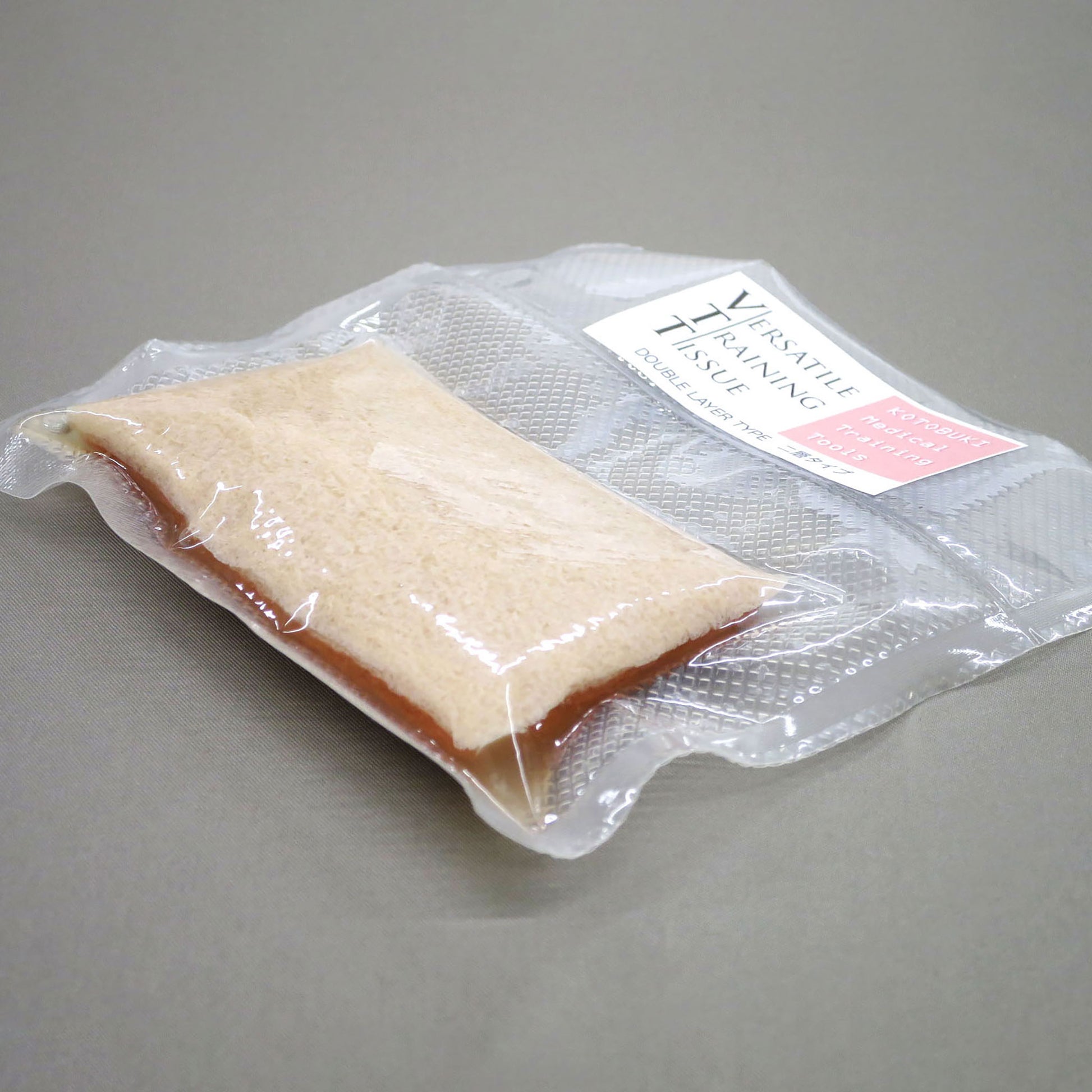 The Double Layer Type in its shrink-wrapped packaging against a grey background. When packaged, it is around 1.5 centimeters thick. 