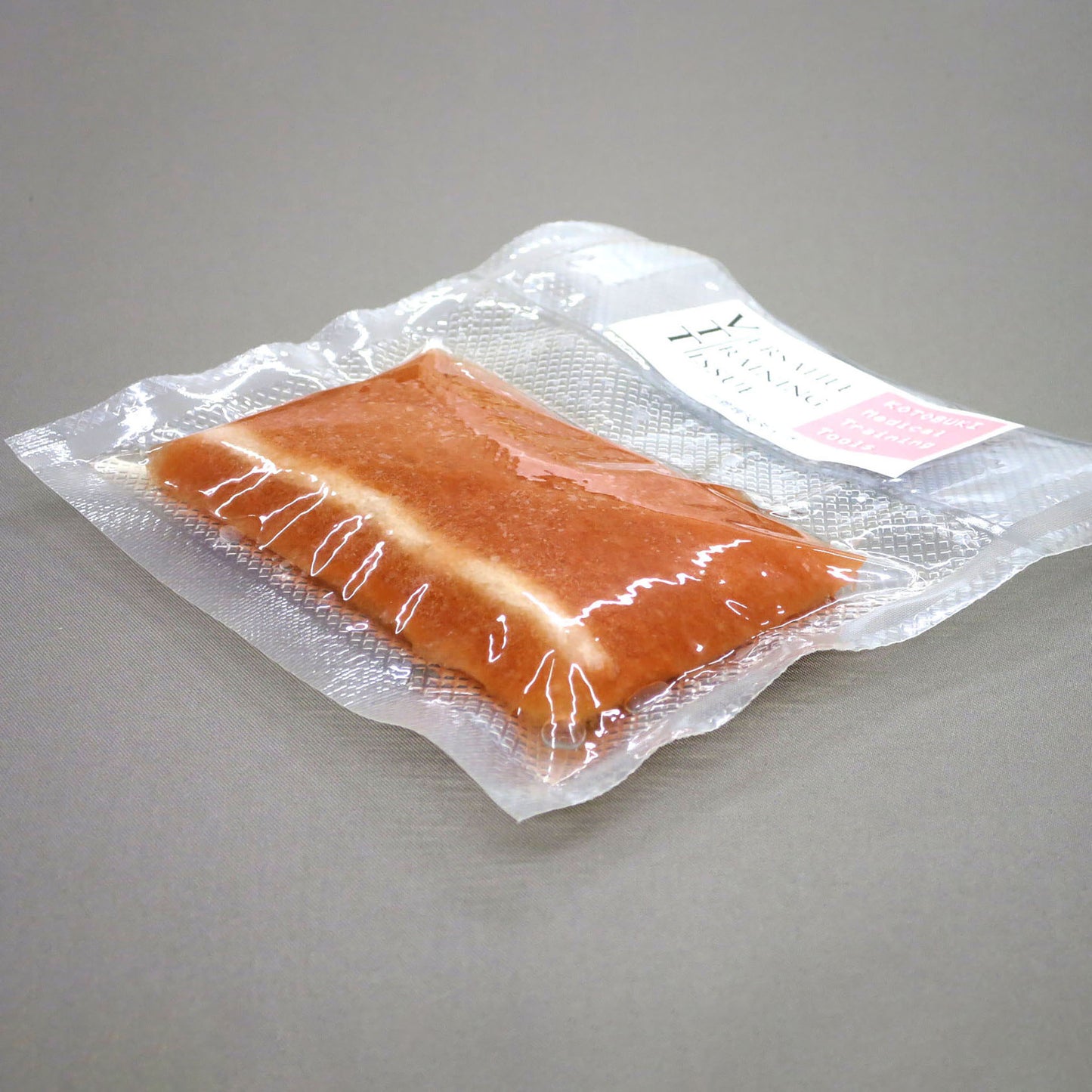 The VTT Vessel Dissection Model in its shrink-wrapped packaging against a gray background. When packaged, it is only about 1.5 centimeters thick. 