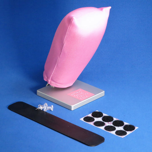 A pink, synthetic vaginal stump model made of fabric and foam is propped at an angle on a silver base. 
